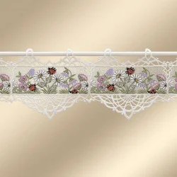Ein Spitzenvolant mit einem Blumenmuster aus Gänseblümchen und Wildblumen in Weiß, Lila und Rosa. Der Volant hat Wellenkanten und dekorative Schlaufen an der Oberseite zum Aufhängen an einer Gardinenstange. Der Hintergrund ist beige.