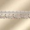 Spitzenbesatz mit einem sich wiederholenden Blumen- und Sternenmuster in Beige- und Goldtönen, verziert mit kleinen Perlen und Stickereien. Die Borte ist auf einem glatten, beigefarbenen Hintergrund mit Farbverlauf angebracht.