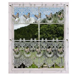 Ein Fenster mit einem hellen Holzrahmen ist mit zwei weißen Spitzenvorhängen mit Schmetterlings- und Blumenmustern versehen. Die filigranen Vorhänge sind teilweise geöffnet und geben den Blick auf die grünen Bäume und den blauen Himmel in der Landschaft draußen frei.