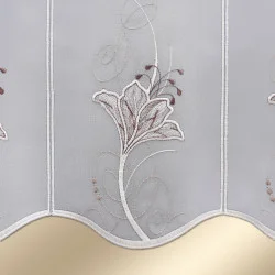 Die Scheibengardine Lilie Braun-Beige ist eine halbtransparente Fenstergardine aus Plauener Spitze mit floraler und ornamentaler Stickerei in Beige- und Brauntönen. Sie hat einen Wellenschliff und ist für die Fensterdekoration gedacht.