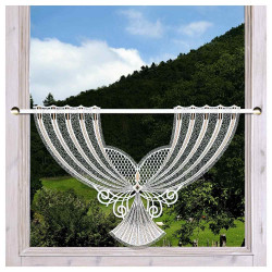 Ein Fenster ist mit einem weißen Spitzenvorhang in der Form eines stilisierten Fächers geschmückt. Die Vorhangstange umrahmt die ausladenden Ornamente, während üppige grüne Hügel und Bäume den malerischen Hintergrund bilden.