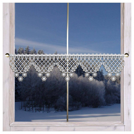 Ein Fenster mit weißem Holzrahmen bietet Ausblick auf eine verschneite Landschaft mit Bäumen und einem gefrorenen Gewässer. Das Fenster ist mit einem dekorativen Spitzenvolant mit einem komplizierten Design und Schneeflockenmustern geschmückt. Der Himmel ist klar und blau und spiegelt die winterliche Szene wider.