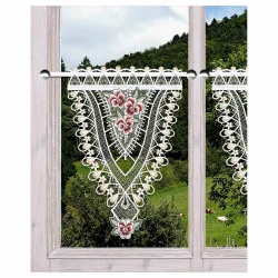 Ein Holzfenster zeigt einen Spitzenvolant mit floralen Mustern. Der Blick nach draußen zeigt eine üppig grüne Landschaft mit Bäumen und einigen grasenden Tieren auf einem Hügel.