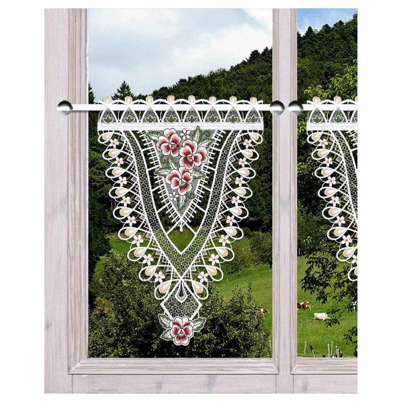 Ein Holzfenster zeigt einen Spitzenvolant mit floralen Mustern. Der Blick nach draußen zeigt eine üppig grüne Landschaft mit Bäumen und einigen grasenden Tieren auf einem Hügel.