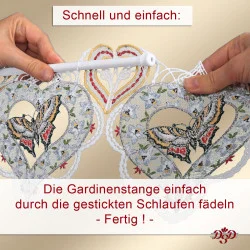 Zwei Hände fädeln eine Gardinenstange durch gestickte Schlaufen an dekorativen Spitzenherzen mit Schmetterlingen. Ein deutscher Text erklärt, wie man die Spitze ganz einfach an den Schlaufen aufhängt.