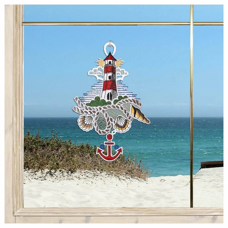 Ein Fenster bietet Blick auf einen Sandstrand und das blaue Meer. Ein farbenfrohes Spitzendekor – gefertigt aus Vogtländischer Spitze – mit einem Leuchtturm, Muscheln und einem roten Anker – verleiht charmanten maritimen Fensterbildern die perfekte Bad-Deko.