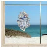 Eine Strandszene, betrachtet durch ein Fenster mit einem dekorativen blau-weißen Meeresornament, bestehend aus Muscheln, Fischen, einem Seestern und einem eleganten Seepferdchen, erzeugt atemberaubende maritime Fensterbilder auf dem Glas.