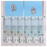 Ein Fenster mit transparenten, dekorativen Scheibengardinen mit Seepferdchen- und Fischmotiven bietet Blick auf einen Sandstrand und das blaue Meer. Zwei gestickte Fensterbilder mit Meeresmotiven hängen am Fenster.