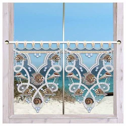 An einem Holzfenster hängen Scheibengardinen mit gestickten Fischen, Muscheln und Algenmustern, die maritime Deko verleihen und den Blick auf einen Sandstrand und das blaue Meer unter einem klaren Himmel einrahmen.