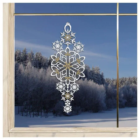 Das Schneeflocken-Ornament aus Spitze mit goldenen und weißen Details hängt in einem Fenster mit Blick auf einen verschneiten Wald und eine gefrorene Landschaft unter einem klaren blauen Himmel.