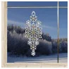 Das Schneeflocken-Ornament aus Spitze mit goldenen und weißen Details hängt in einem Fenster mit Blick auf einen verschneiten Wald und eine gefrorene Landschaft unter einem klaren blauen Himmel.