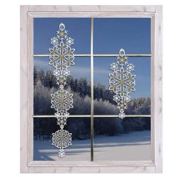 Ein frostiges Fenster mit zwei hängenden Schneeflocken-Fensterbildern, mit Blick auf eine verschneite Landschaft mit einem Wald von schneebedeckten Bäumen unter einem klaren blauen Himmel.