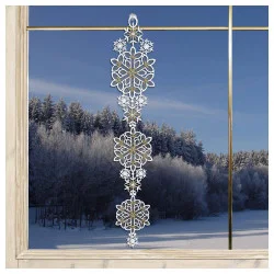 Eine dekorative Giralnde aus gestickten weißen Schneeflocken hängt in einem Fenster, aus dem ein verschneiter Wald und ein blauer Himmel zu sehen sind.