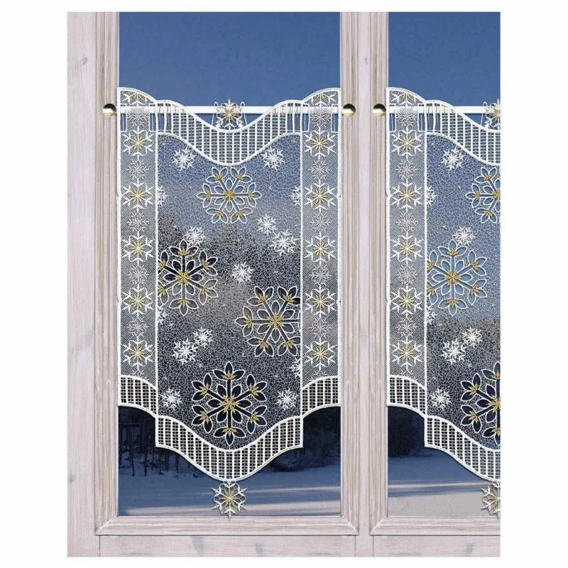 Ein weißer Spitzenvorhang mit goldenen und weißen Schneeflockenmustern hängt an einer Stange über einem Fenster. Der Fensterrahmen ist aus hellem Holz, und im Hintergrund ist eine verschneite Szene im Freien zu sehen.