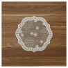 cEin rundes, dekoratives Spitzendeckchen mit weißen Schneeflockenmustern und einem Wellenrand liegt auf einer Holzoberfläche mit naturbrauner Maserung.