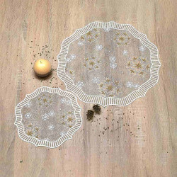 Zwei runde Spitzendeckchen mit floralen Mustern liegen auf einer Holzfläche. Ein Apfel und zwei Tannenzapfen liegen in der Nähe, und auf dem Tisch sind kleine Samen verstreut.