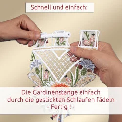 Zwei Hände fädeln eine Gardinenstange durch die bestickten Schlaufen eines dekorativen Spitzenvorhangs mit bunten Blumenmustern. Der deutsche Text erklärt, dass der Vorgang schnell und einfach ist.