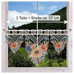 Ein dekorativer Spitzenvorhang mit bunten Blumenmustern hängt an einem Fenster. Eine Messlinie mit Pfeilen zeigt die Breite von etwa 57 cm an. Außerhalb des Fensters sind grüne Hügel und Bäume zu sehen.