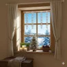 Ein gemütliches Fenster, dekoriert mit weißen Vorhängen, hängendem Schneeflockenschmuck, Kerzen, einem kleinen Tannenbaum und einem Korb. Draußen sorgen schneebedeckte Bäume und ein strahlend blauer Himmel für eine winterliche Stimmung.