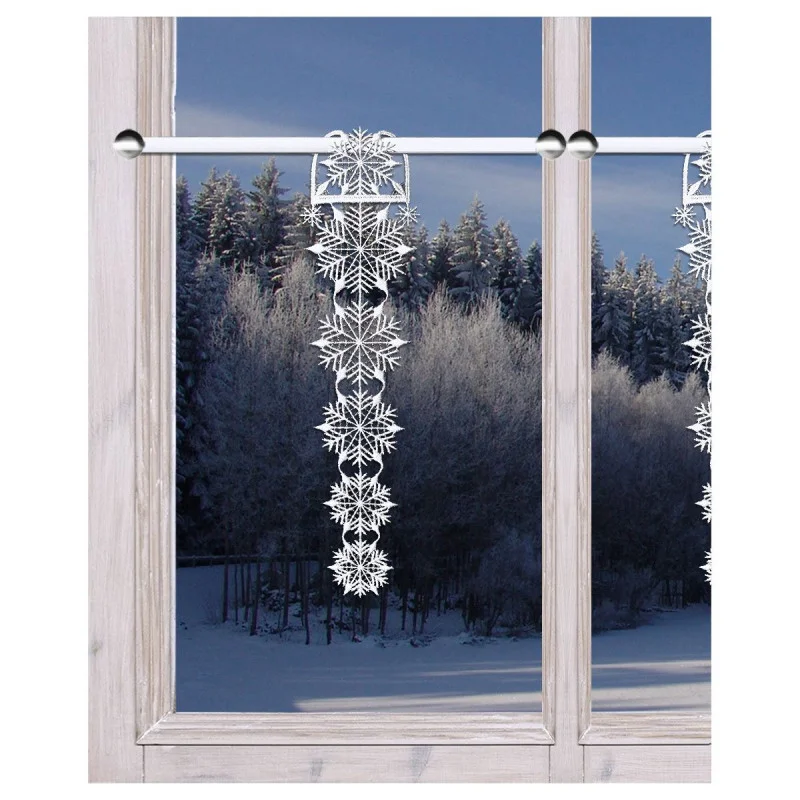 Eine frostige Winterszene, die durch ein Fenster betrachtet wird, mit verschneiten Bäumen draußen und einer hängenden Girlande mit dekorativen weiß-silbernen Schneeflocken, die innen an einer Gardinenstange befestigt ist.