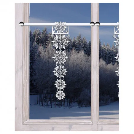 Eine frostige Winterszene, die durch ein Fenster betrachtet wird, mit verschneiten Bäumen draußen und einer hängenden Girlande mit dekorativen weiß-silbernen Schneeflocken, die innen an einer Gardinenstange befestigt ist.