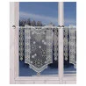 Ein Fenster mit gesticken weißen Vorhängen aus Schneeflocken und Sternenmustern, wobei draußen ein verschneiter Wald zu sehen ist. Die Vorhänge sind an einer Stange aufgehängt und haben an den Rändern dekorative Ausschnitte.