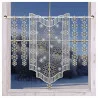 Ein Fenster mit Milchglas und Spitzenvorhängen mit verschlungenen Schneeflockenmustern, umrahmt von einer verschneiten Landschaft mit Bäumen und einem klaren Himmel.