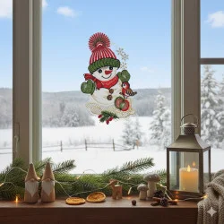 Eine festliche Fensterdekoration zeigt ein Fensterbild Schneemanns auf der Glasscheibe, während draußen schneebedeckte Bäume stehen. Kerzenlaternen, Tannenzweige, Holzzwerge und Pilze auf der Fensterbank schaffen eine gemütliche Winterszene.