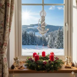 Ein festliches Fensterbild: Eine Fensterbank mit vier roten Kerzen in einem Tannenkranz, kleinen Engelsfiguren, Plauener Spitze und Lichterketten geschmückt. Draußen glitzern verschneite Tannenbäume in der strahlenden Sonne.