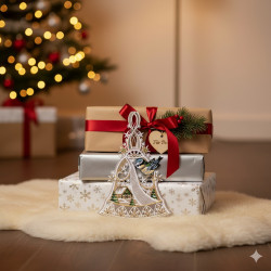 Drei eingepackte Weihnachtsgeschenke auf einem weißen, flauschigen Teppich vor einem geschmückten Weihnachtsbaum gestapelt. Das oberste Geschenk ist mit einer roten Schleife, einem Tannenzweig, einem Herzanhänger und einem Plauener Spitze Fensterbild Glocke mit Vögelchen als charmante Winterdekoration versehen.