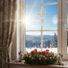 Eine sonnenbeschienene Schneelandschaft ist durch ein Fenster zu sehen, das mit einem Plauener Spitze Fensterbild Schneeflocke geschmückt ist. Auf der Fensterbank sorgt ein Weihnachtskranz mit vier roten Kerzen, Lichterketten und zwei Engelsfiguren für gemütliches Winterflair.