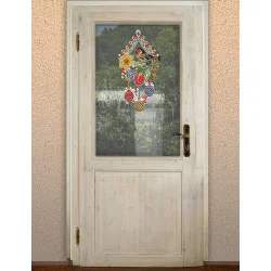 Eine helle Holztür mit einer oberen Glasscheibe zeigt das "Fensterbild Stieglitz mit Frühlingsblüten blau Plauener Spitze Ostern", ein hängendes Ornament, das einen Vogel und Frühlingsblumen darstellt. Durch die Glasscheibe ist grünes Laub zu sehen