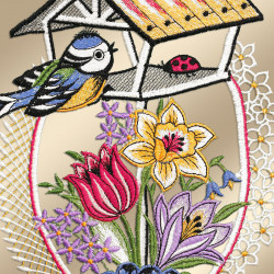 Das Fensterbild Frühlingsgezwitscher Plauener Spitze zeigt einen gestickten Vogel auf einem Futterhäuschen, in dessen Nähe ein roter Marienkäfer sitzt. Darunter befinden sich gestickte Darstellungen einer gelben Narzisse, einer rosa Tulpe und eines violetten Krokus zwischen grünen Blättern