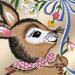 Detaillierte Stickerei eines braunen Kaninchens, das ein rosa gepunktetes Halstuch trägt und blaue und rosa Blumenstiele hält. Weiße Lilien und gelbe Blumen umgeben es. Der Hintergrund ist in einem weichen, hellen Beigeton gehalten. Die Stickerei ist dicht und farbenfroh und verleiht dem Ganzen Struktur.