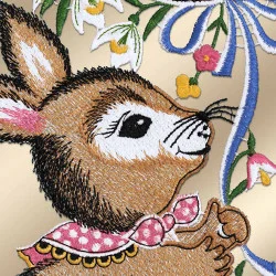 Detaillierte Stickerei eines braunen Kaninchens, das ein rosa gepunktetes Halstuch trägt und blaue und rosa Blumenstiele hält. Weiße Lilien und gelbe Blumen umgeben es. Der Hintergrund ist in einem weichen, hellen Beigeton gehalten. Die Stickerei ist dicht und farbenfroh und verleiht dem Ganzen Struktur.