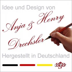 Eine Hand, die einen Stift hält, schreibt "Anja &amp; Henry Drechsler" in eleganter roter Schrift. Darüber und darunter steht in grauer Schrift: "Idee und Design von" und "Hergestellt in Deutschland". Am unteren Rand erscheinen ein Logo und Pinselstriche in den Farben der deutschen Flagge.