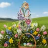 Ein Fensterbild Frühlingsfreude Plauener Spitze mit floralen Motiven in Form einer großen verschnörkelten "8" steht aufrecht im grünen Gras. In der Nähe steht ein Weidenkorb mit pastellfarbenen Ostereiern, Tulpen, Narzissen und Glockenblumen auf einer sonnenbeschienenen Frühlingswiese.