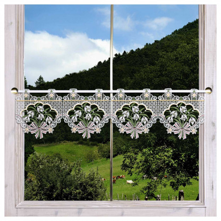 Ein Fenster mit einem weißen Spitzenvorhang mit Blumen- und Blattmustern hängt zu einem Drittel an der Scheibe. Durch das Fenster sieht man eine grüne Wiese mit grasenden Kühen, Bäumen, Sträuchern und einem bewaldeten Hügel unter einem bewölkten Himmel.