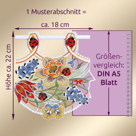 Ein besticktes Spitzenstück mit floralen Motiven in Gelb, Blau und Rot, darunter Marienkäfer und Lilien. Das Stück hat eine Höhe von ca. 22 cm und eine Breite von ca. 18 cm und ist neben einem lila DIN A5-Blatt ausgestellt. Der deutsche Text gibt die Maße an.