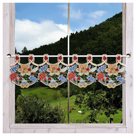 Ein Fenster mit einem Spitzenvorhang, der mit gestickten Blumen und Blättern verziert ist. Hinter dem Fenster befindet sich eine Landschaft mit grünem Gras, Bäumen, Hügeln und grasenden Kühen unter einem Himmel, der teilweise von Wolken bedeckt ist.