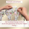 Zwei Hände führen eine weiße Gardinenstange durch die bestickten Schlaufen eines dekorativen Spitzenvorhangs mit Blumen- und Kaninchenmustern. Über und unter dem Bild erscheint ein deutscher Text mit der Anweisung, dass der Vorhang durch Einfädeln der Stange durch die Schlaufen angebracht wird.