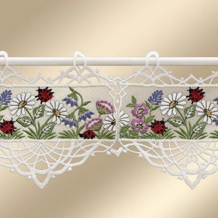 Ein Spitzenvolant mit gestickten Gänseblümchen, violetten Blüten, grünen Blättern und roten Marienkäfern hat einen gewellten Rand mit detaillierter weißer Spitzenarbeit. Er ist an einer weißen Stange vor einem beigen Hintergrund angebracht.