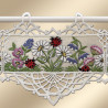 Ein Wandbehang aus Spitze mit gestickten Gänseblümchen, lila und rosa Blumen, grünen Blättern und mehreren roten und schwarzen Marienkäfern. Der Wandbehang ist mit einer detaillierten weißen Spitzenbordüre versehen und wird an einer weißen Stange mit drei Schlaufen aufgehängt.