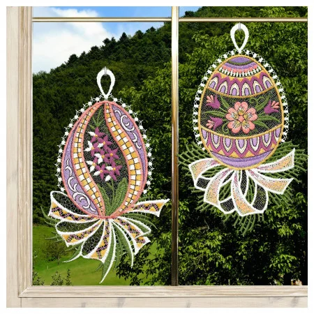 Zwei gestickte Ostereier, verziert mit floralen und geometrischen Mustern in verschiedenen Farben, hängen an einem Fenster. Jedes Ei hat eine weiße Spitzenschleife und eine bandartige Spitze am unteren Ende. Durch das Fenster sind grüne Hügel, Bäume, blauer Himmel und Wolken zu sehen.