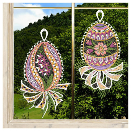 Zwei gestickte Ostereier, verziert mit floralen und geometrischen Mustern in verschiedenen Farben, hängen an einem Fenster. Jedes Ei hat eine weiße Spitzenschleife und eine bandartige Spitze am unteren Ende. Durch das Fenster sind grüne Hügel, Bäume, blauer Himmel und Wolken zu sehen.