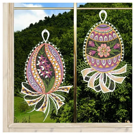 Zwei gestickte Ostereier, verziert mit floralen und geometrischen Mustern in verschiedenen Farben, hängen an einem Fenster. Jedes Ei hat eine weiße Spitzenschleife und eine bandartige Spitze am unteren Ende. Durch das Fenster sind grüne Hügel, Bäume, blauer Himmel und Wolken zu sehen.