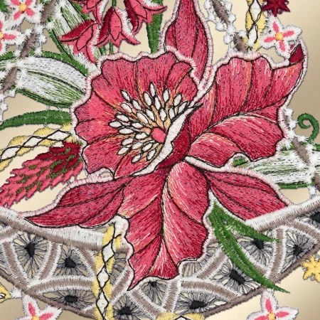 Stickerei mit einer auffälligen roten Blume mit weißen Staubgefäßen und grünen Blättern, umgeben von kleineren Blumen und komplizierten Spitzenmustern in Creme, Gelb und Schwarz auf beigem Hintergrund. Die Nähte und verschiedenen Stoffstrukturen sind deutlich sichtbar.