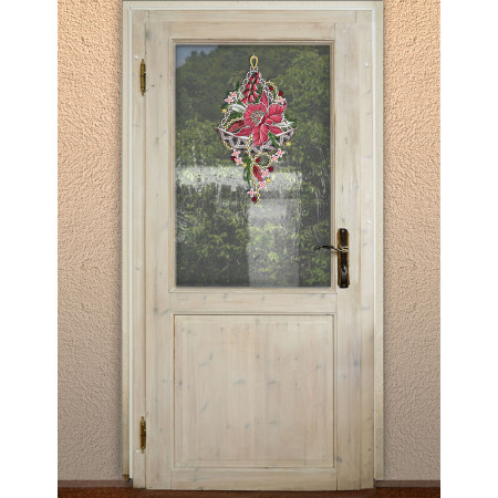 Eine helle Holztür ist in der oberen Hälfte mit einer Glasscheibe versehen, an der ein rosa und rotes, mit Blumen verziertes Schmetterlingsornament hängt. Draußen sind durch die Scheibe grüne Bäume und Pflanzen zu sehen. Die Tür ist mit einem Messinggriff ausgestattet.