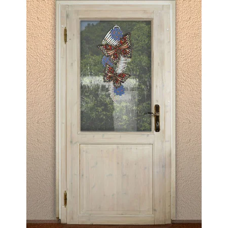 Eine helle Holztür mit einem Glasfenster gibt den Blick auf eine Naturszene im Freien frei. An der Glasscheibe ist ein Schmetterlingswindspiel aus Metall und Perlen angebracht, das drei Schmetterlinge mit detaillierten Mustern in Rot, Blau und Silber zeigt.