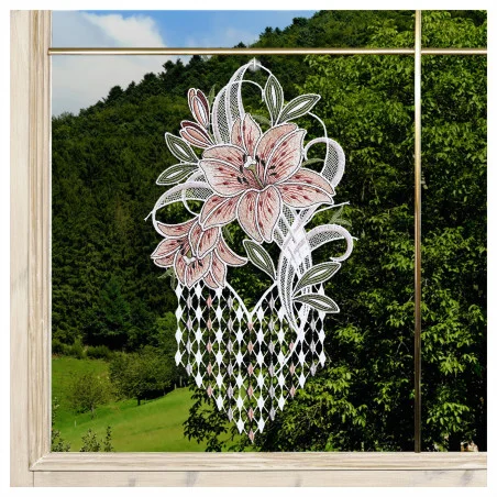Eine Fensterdekoration aus Spitze mit rosa und weißen Blumen und grünen Blättern ist auf einer Fensterscheibe abgebildet. Das Fenster hat einen hellen Holzrahmen. Durch das Glas sind sanfte grüne Hügel, Bäume und ein blauer Himmel mit vereinzelten Wolken zu sehen.